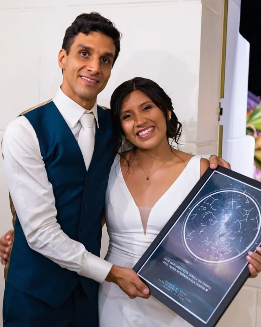 Noivos sorrindo com o quadro do mapa das estrelas do dia do casamento