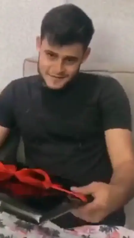 Rapaz sorrindo ao abrir o presente com laço vermelho